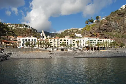 White waterfront buildings beneath Ponta do Sol’s cliffs, along the seafront walking route.